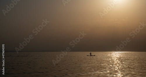 Silhouette of unrecognizable woman in wetsuit paddling on a SUP board. Female floating on a stand up paddle board in the gulf. Summer season and active leisure concept. Dynamic recreation.