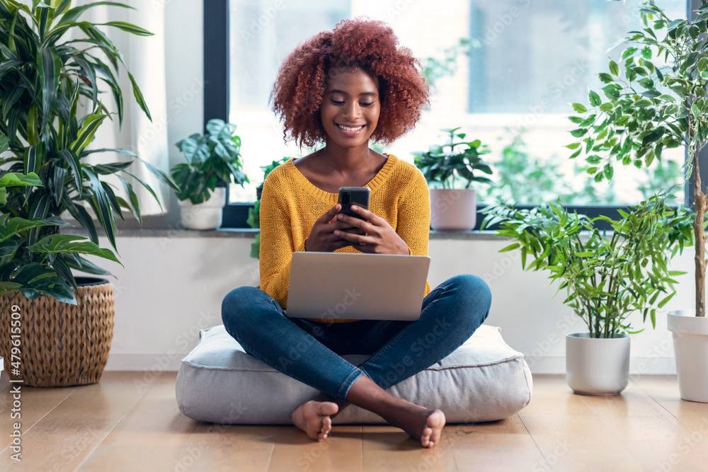 Pretty woman using her mobile phone while working with laptop sitting on a puff at home. Pretty woman using her mobile phone while working with laptop sitting on a puff at home.