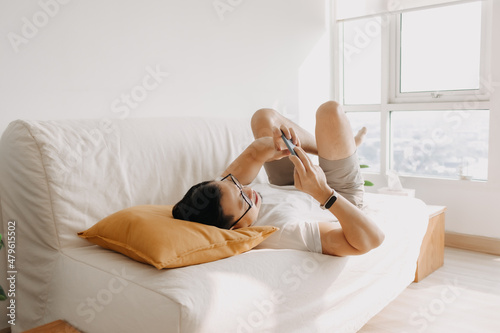 Adult Asian man is having fun to play mobile game in the living room apartment.
