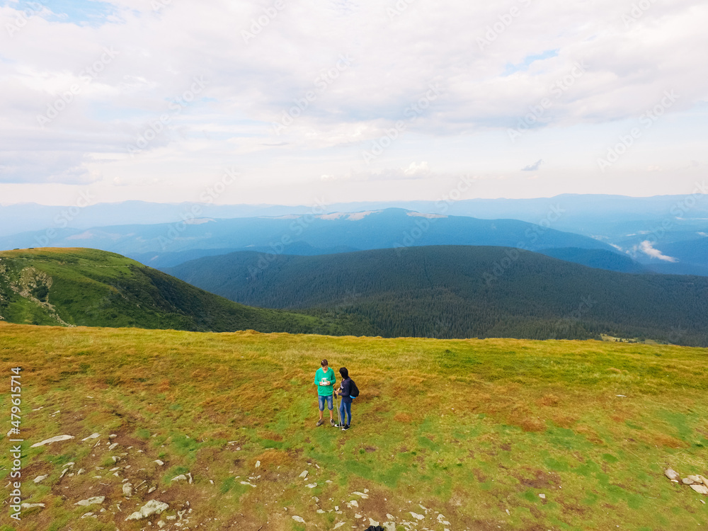 Aerial view of the Great Green Ridge. Guy and Girl Standing on a Big Hill against the Backdrop of a Huge Mountain Landscape