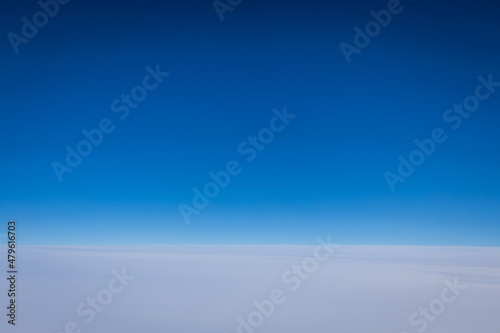 The of a clear blue sky with a very flat featureless cloudy sky below as viewed from the window of a jet.