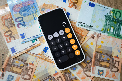 Smartphone is open in the calculator application and lies on the money. Cash in euros for payment or exchange. A man calculates his salary in euro banknotes. Saving money, withdrawing a bank deposit. 