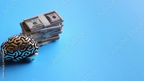 Business minded concept. Brain model and stack of money on blue background with copy space