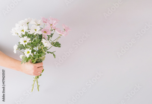 Creative spring arrangement made of a bouquet of flowers in hand on a gray background. Minimal concept with copy space.