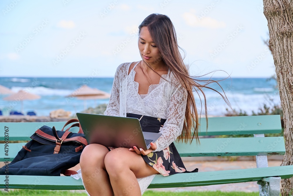 Beautiful young Asian woman using laptop sitting on an outdoor bench
