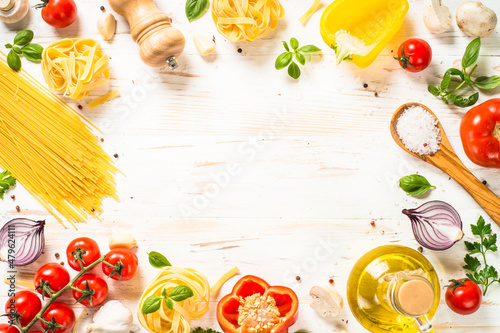 Italian food background on white kitchen table. Raw Pasta, olive oil, spices, tomatoes and basil. Food frame. Top view with copy space.