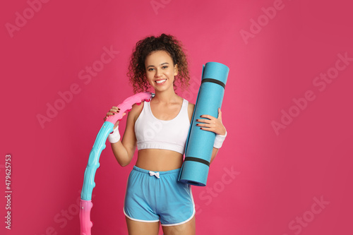 Beautiful African American woman with yoga mat and hula hoop on pink background photo