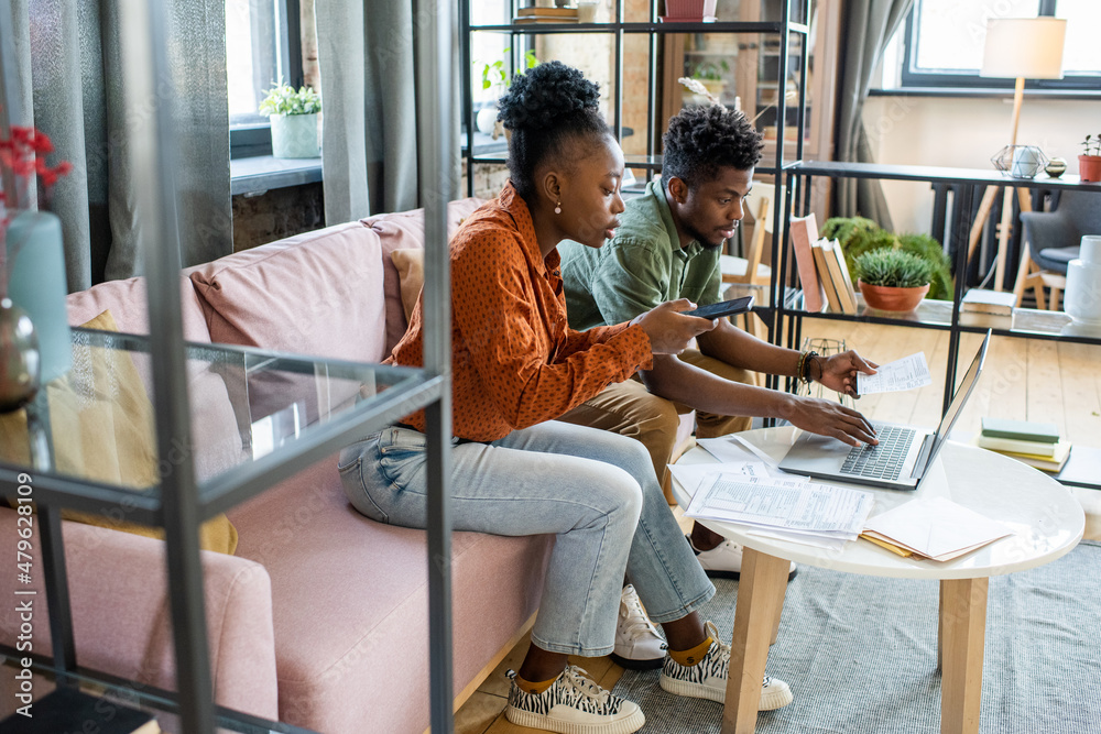 Obraz premium Two young contemporary coworkers working with mobile gadgets and financial data while sitting on couch by table