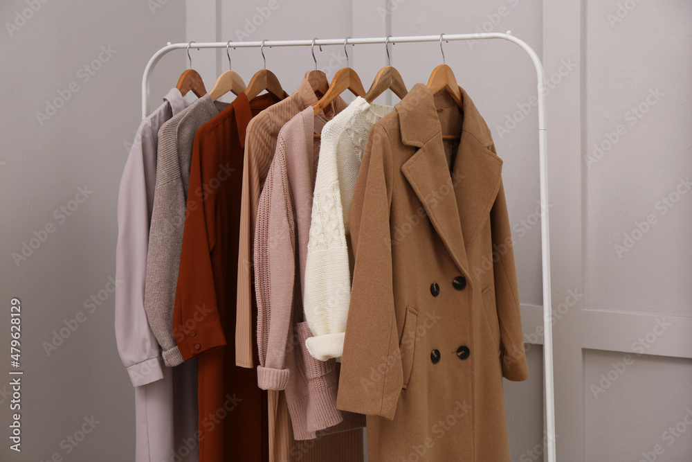 Rack with different stylish clothes near grey wall indoors Rack with different stylish clothes near grey wall indoors