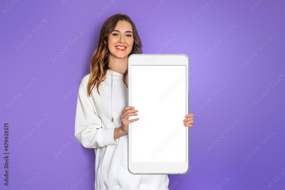 Mobile App. Caucasian young woman wearing white hoodie smiling and holding big smartphone with blank white screen, copy space for Design. Mockup Mobile App. Caucasian young woman wearing white hoodie smiling and holding big smartphone with blank white screen, copy space for Design. Mockup