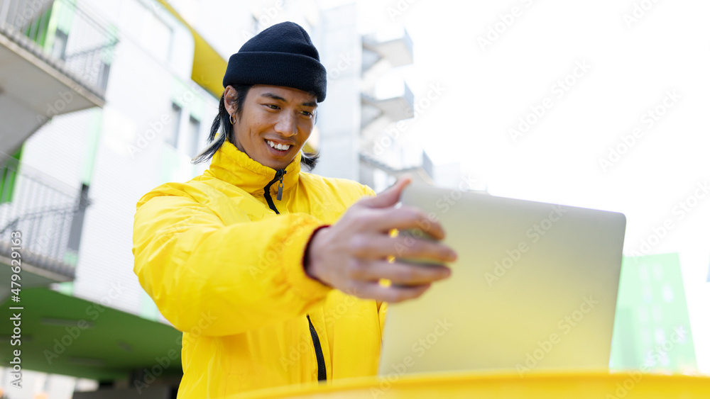 Positive Asian man browsing laptop on street Positive Asian man browsing laptop on street