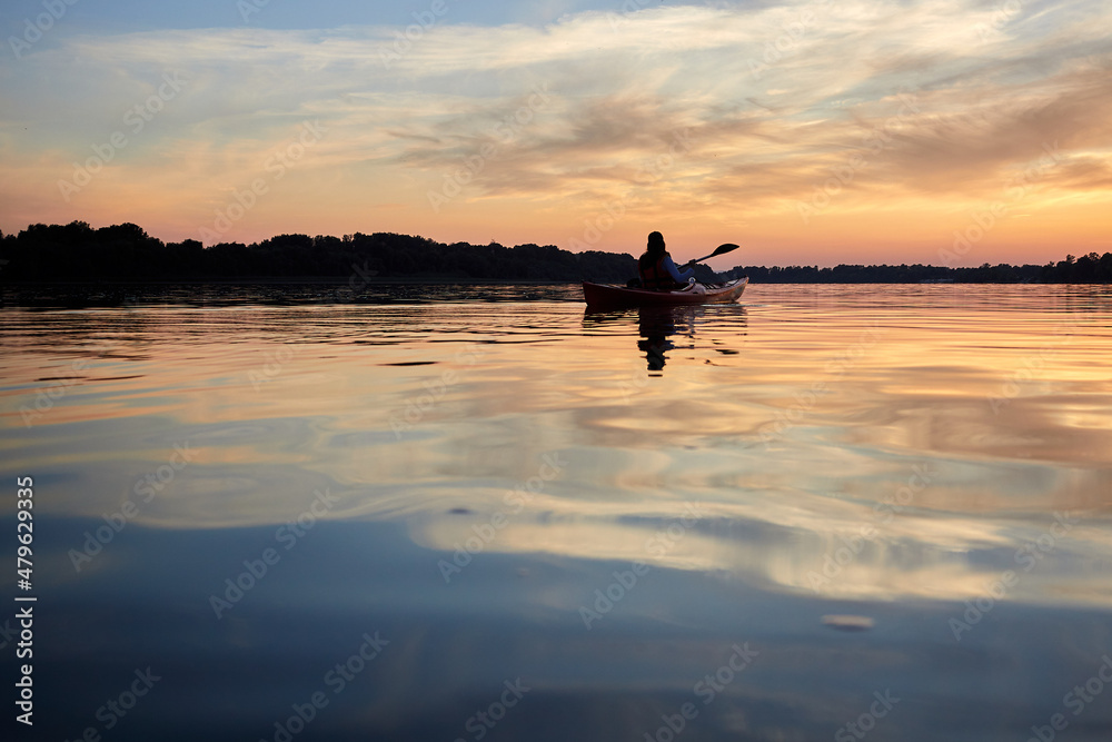 Sillouette of woman kayaking on river at golden sunset. Summer time, active recreation. Healthy lifestyle and care about mental health, resting in privacy and peace