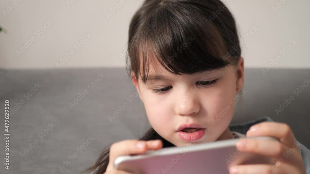 Cute little kid girl holding smart phone enjoying using mobile apps, playing games at home. Small child learning in cellphone, watching video. Mobile technology concept. Cute little kid girl holding smart phone enjoying using mobile apps, playing games at home. Small child learning in cellphone, watching video. Mobile technology concept.