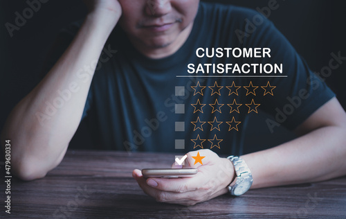 Customer dissatisfaction experience concept, business male customer hand-holding head, disappointed with bad service, by rating through smartphone, bad review, low rating, no service mind. photo