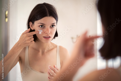 Girl applies cream on her face.
