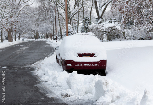 Snow plow clears street around parked car