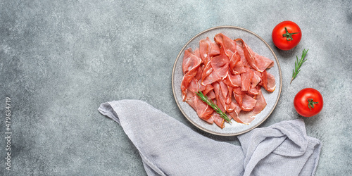 Slices of prosciutto crudo parma or jamon serrano on gray grunge background. Top view, flat lay. Banner photo