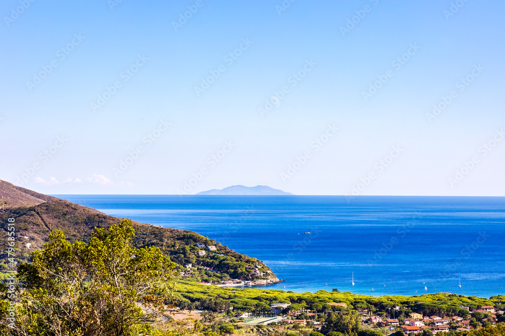 View over the village of Marina del Campo and the blue sea to the island of Monte Christo on the island of Elba in Italy under a bright blue sky in summer