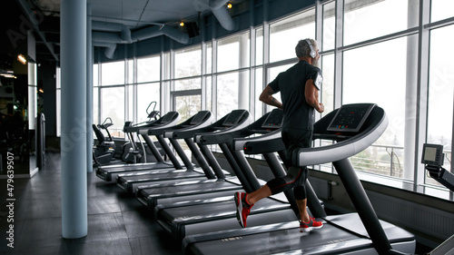 Fotografija Man listening to music via headphones and running on treadmill