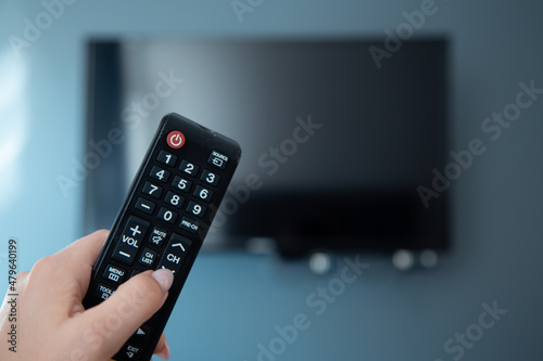 Man hand holds remote control to change channels on big tv plasma display panel. Smart interior design of living room.