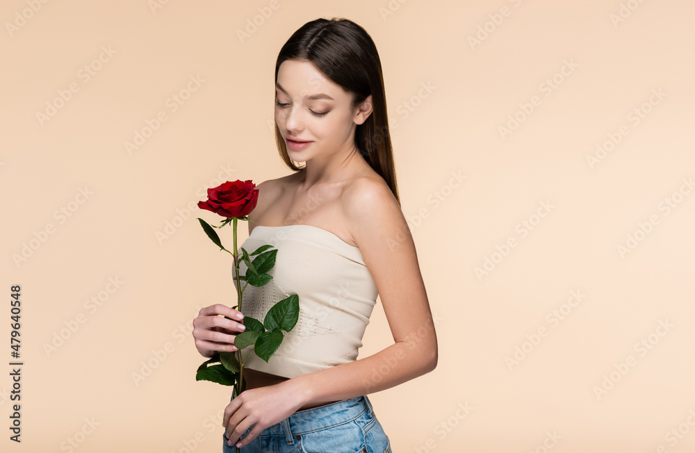 brunette young woman with bare shoulders looking at red rose isolated on beige brunette young woman with bare shoulders looking at red rose isolated on beige