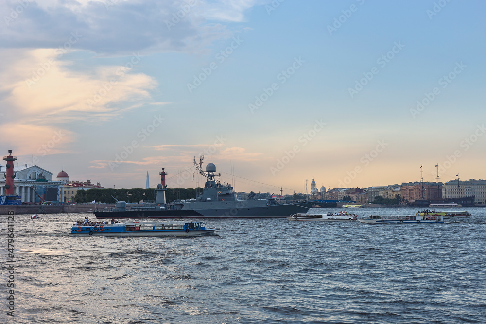 Russian military ship on the Neva in the center of the city surrounded by pleasure boats with tourists against the background of a blue sky