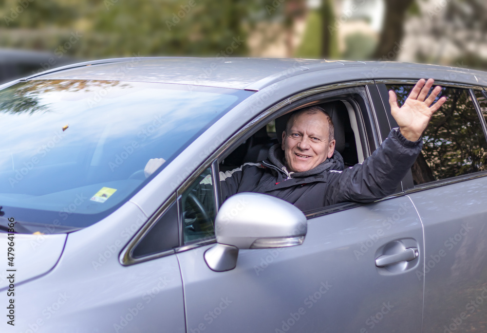 smiling happy elderly man, 60 years old, sitting in car and waving