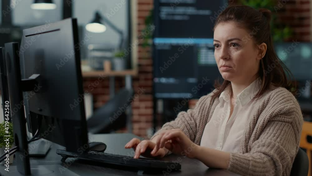 Database programer working focused looking at computer screen while typing in it startup office. App developer writing artificial intelligence code with algorithms compiling on screens in background.