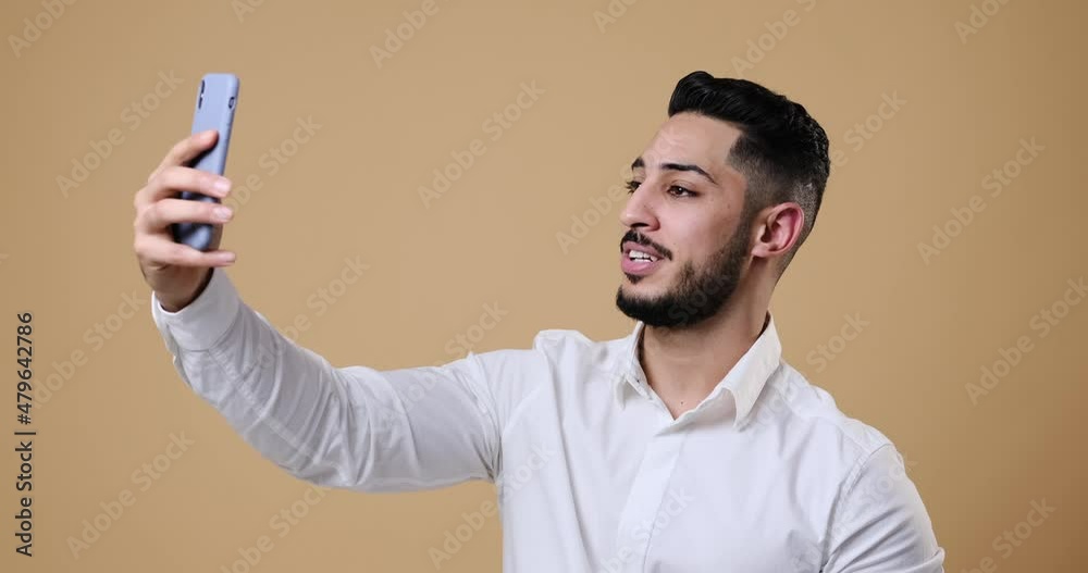 Young businessman video chatting on mobile phone over beige background