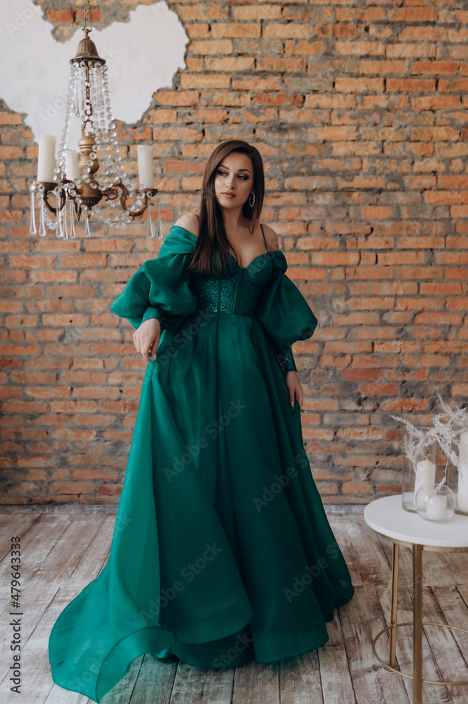 A beautiful girl in a green dress smile shows a brick wall dress