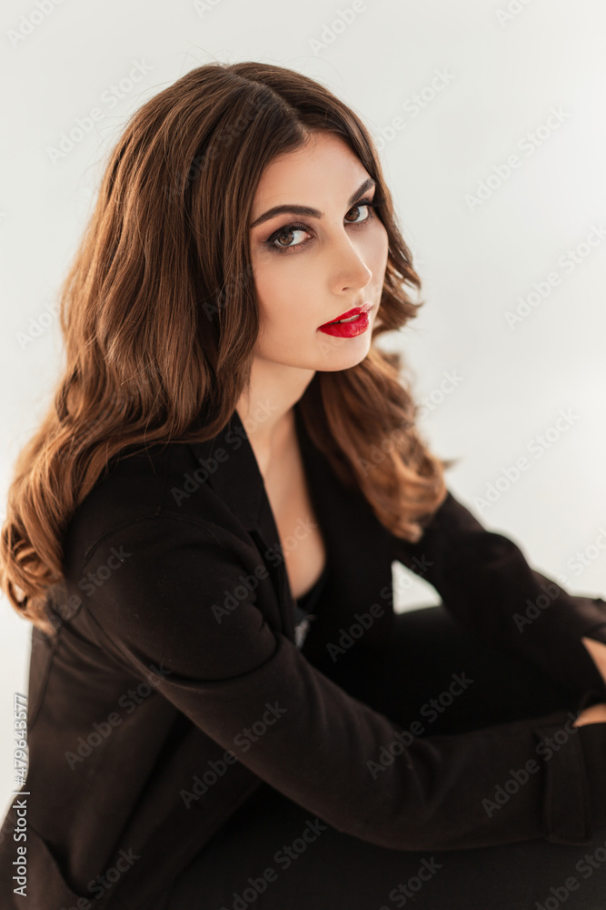 Fototapeta premium Stylish beautiful young woman model with red lips and hairstyle in a black elegant clothes suit on a white background