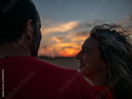A romantic young couple looking at each other knowingly at the sunset on the beach photo