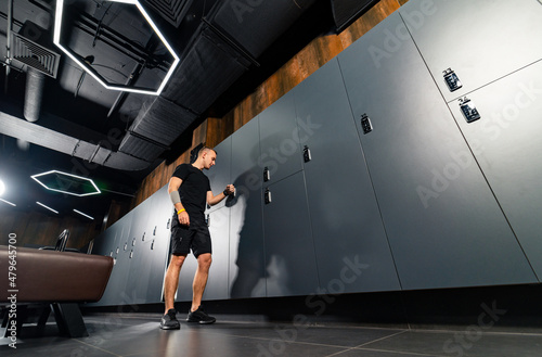 Fotografie, Obraz Young athletic caucasian man standing alone in dark gym locker room and resting
