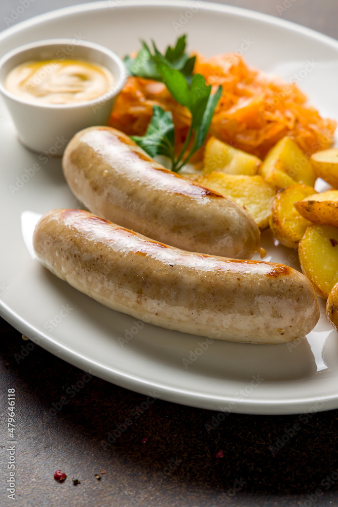 bavarian sausages with potatoes and fried cabbage on plate on dark brown concrete table close up bavarian sausages with potatoes and fried cabbage on plate on dark brown concrete table close up