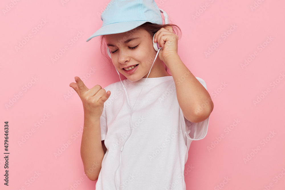 Portrait of happy smiling child girl headphones in a white t-shirt and a cap pink background Portrait of happy smiling child girl headphones in a white t-shirt and a cap pink background