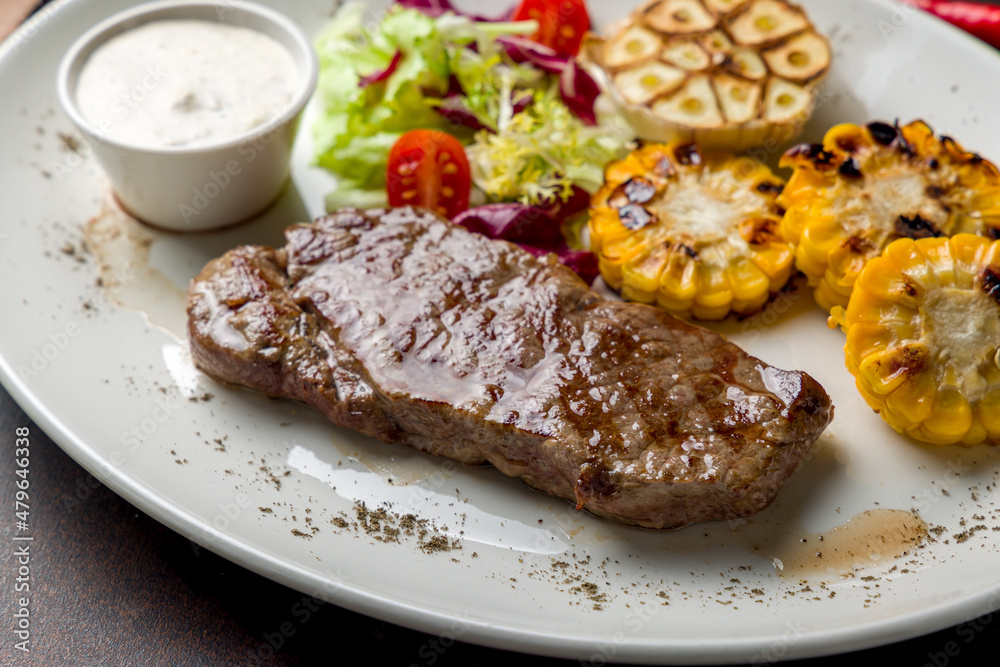 juicy Striploin Steak with fried corn on white plate on dark brown table macro close up