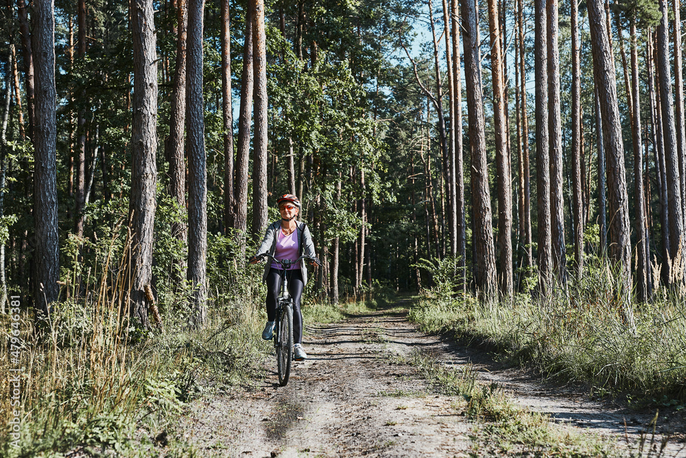 Active woman cycling on forest road. Female riding bicycle off-road route on summer vacation day. Woman wearing bicycle helmet and gloves Active woman cycling on forest road. Female riding bicycle off-road route on summer vacation day. Woman wearing bicycle helmet and gloves