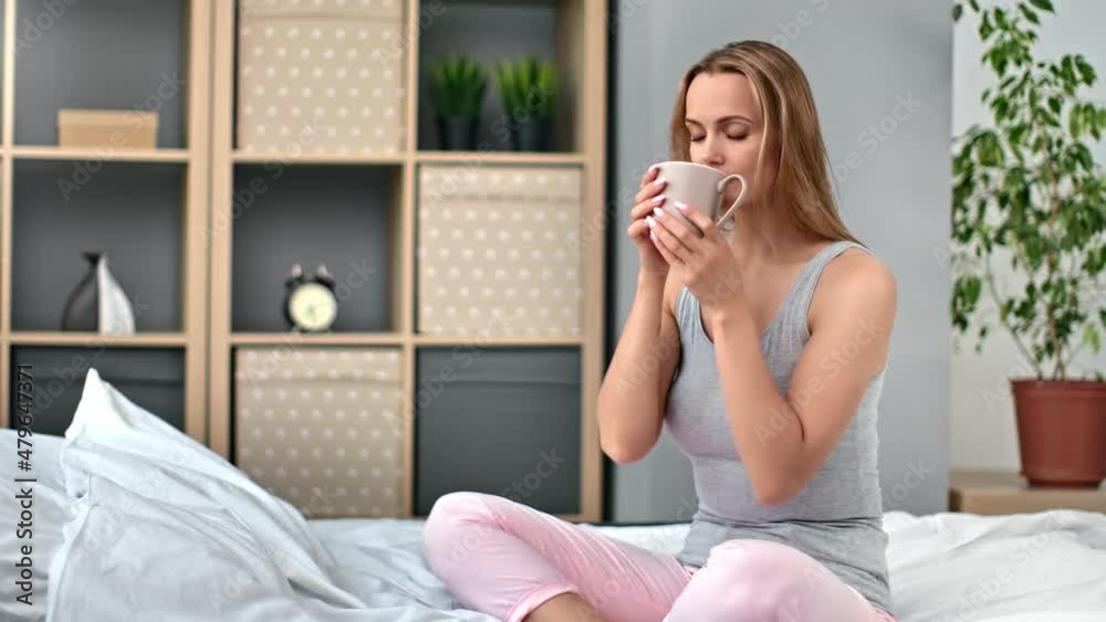 Happy blonde woman drinking hot tea sitting on bed relaxing stress free balance harmony recreation Happy blonde woman drinking hot tea sitting on bed relaxing stress free balance harmony recreation
