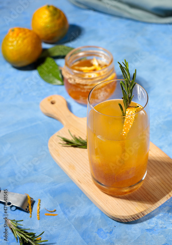 Citrus tea with yuzu zest in a glass and fruit on the table on blue background. Contrast frame, hard shadows, vertical