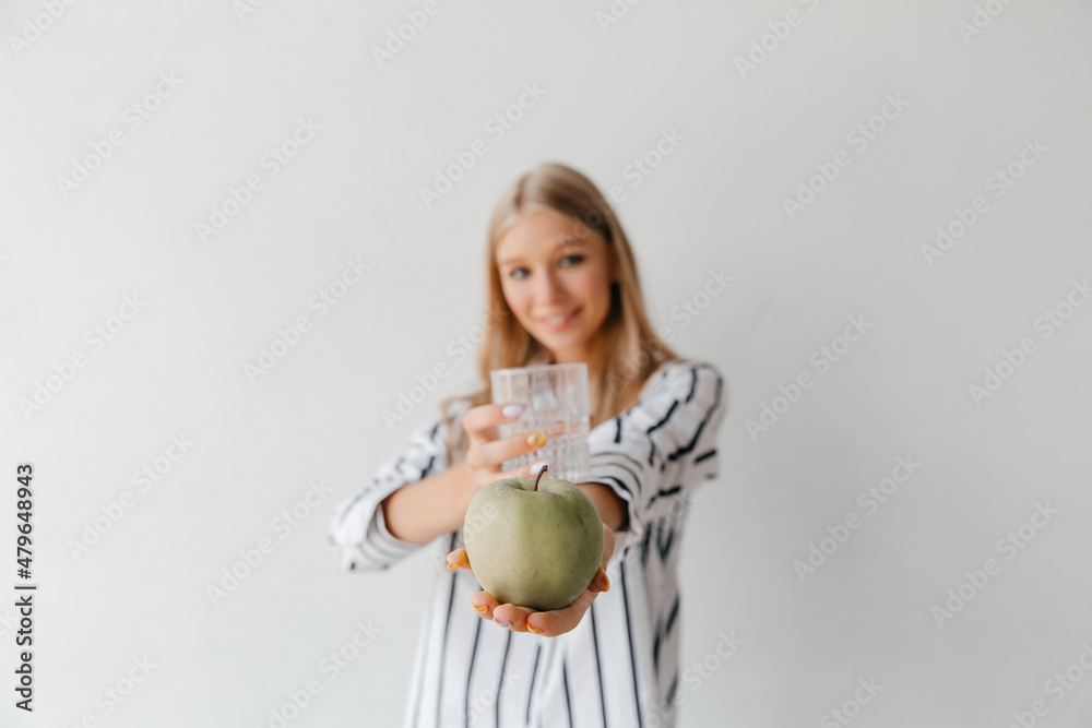 Portrait of a young blonde woman offering an apple and a glass of water, selective focus Portrait of a young blonde woman offering an apple and a glass of water, selective focus