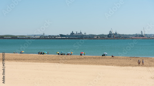 People sunbathing on the beach with the Rota military base in the background, Cadiz, Andalusia, Spain