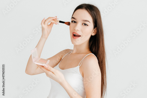 Portrait of beautiful girl making makeup with contouring palette with bronzer, highlighter and a blush, wanting to make perfect makeup isolated over white color background