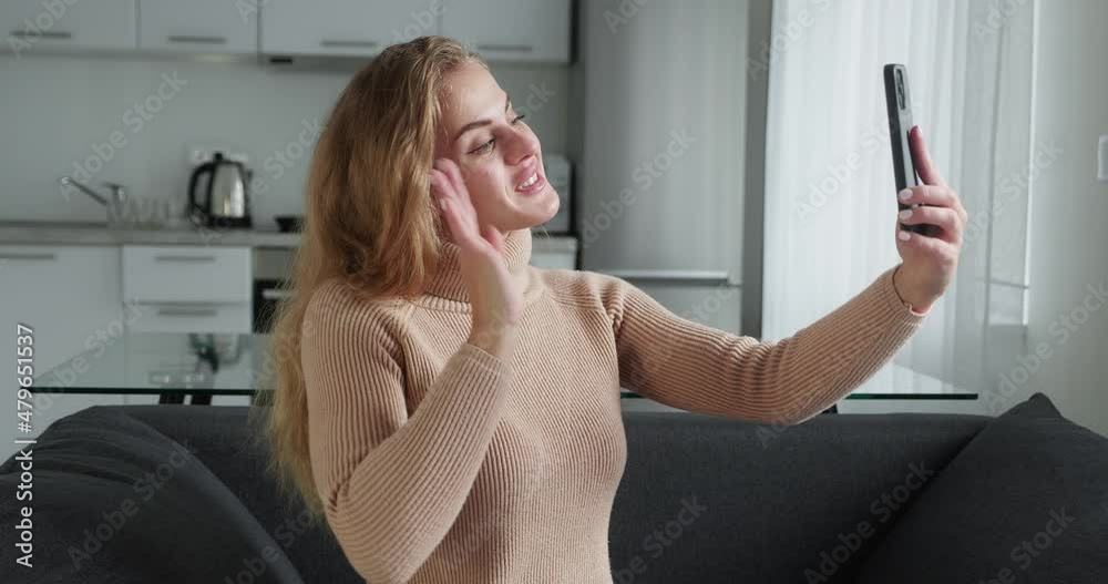 Online conference from home on kitchen background. Young pretty blonde woman of Caucasian appearance in a woolen sweater with is talking on video link using mobile phone and is emotionally happy Online conference from home on kitchen background. Young pretty blonde woman of Caucasian appearance in a woolen sweater with is talking on video link using mobile phone and is emotionally happy
