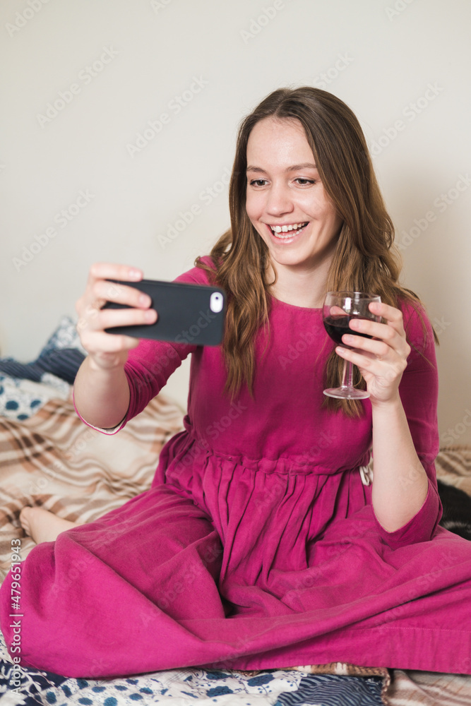 Young millennial woman in pink dress with long hair drink wine and makes a selfie with her black and white tuxedo cat at home. Young millennial woman in pink dress with long hair drink wine and makes a selfie with her black and white tuxedo cat at home.
