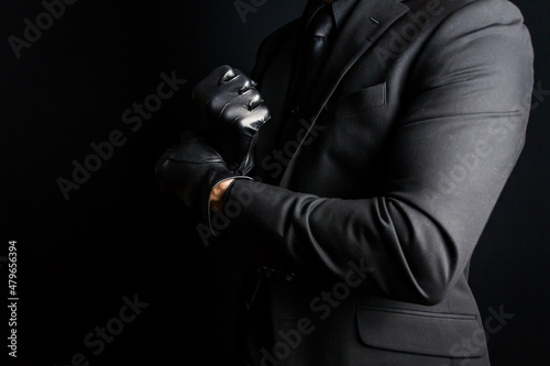 Portrait of Strong Man in Dark Suit Pulling on Black Leather Gloves Menacingly. Concept of Mafia Hitman or Gentleman Assassin. photo