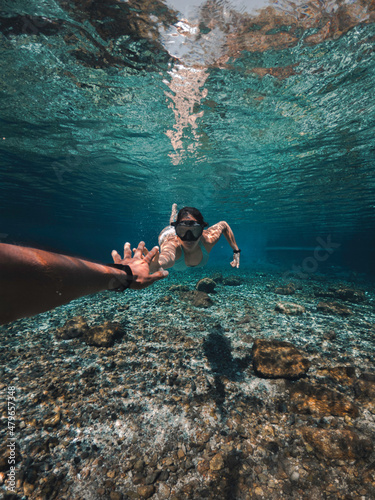 Pareja de freedivers nadando bajo el agua, en un río cristalino, extendiéndose para tomarse de las manos photo