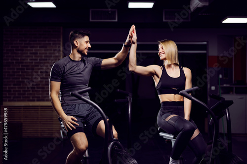 Sporty couple on exercise bikes in a gym accomplished a goal. Teamwork concept.
