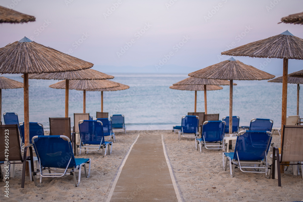 Rows of umbrellas and empty sunbeds on the beach, early in the morning. Nea skioni, Greece. Amazing summer seascape of Adriatic sea. Travel and leisure concepts.