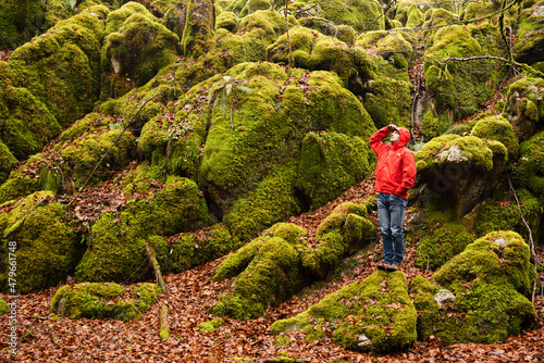 Man wearing a red jacket in a green mossy forest. photo