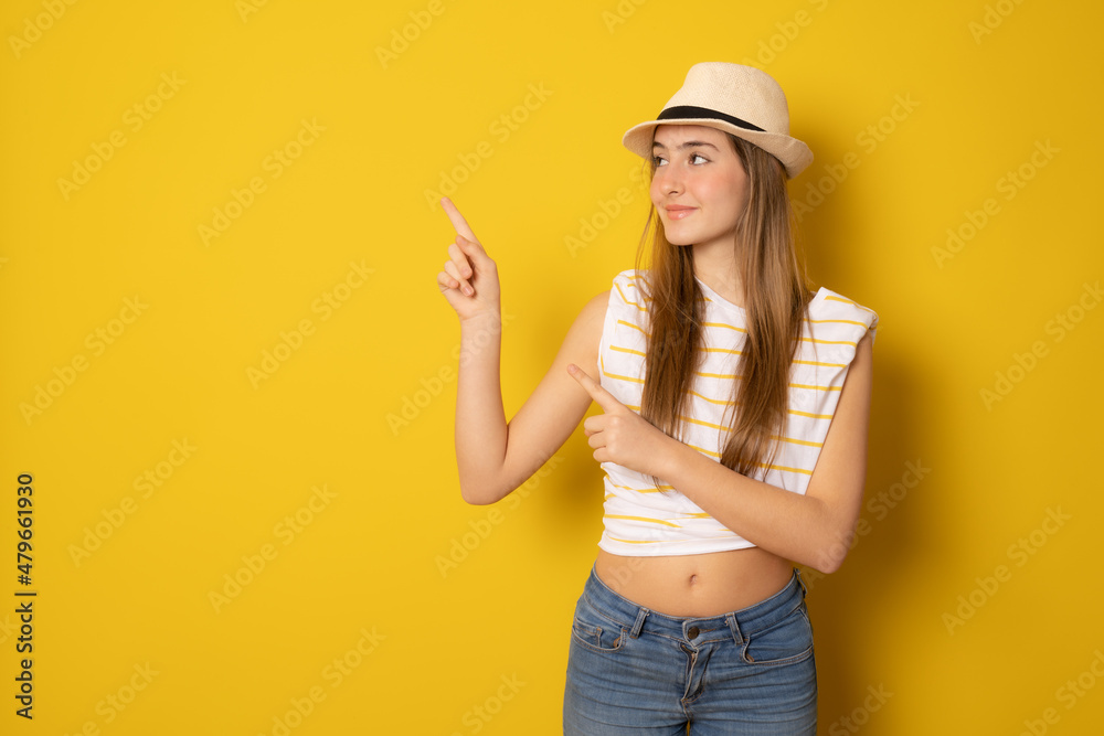 Young woman wearing straw hat pointing fingers up isolated over yellow background. Young woman wearing straw hat pointing fingers up isolated over yellow background.